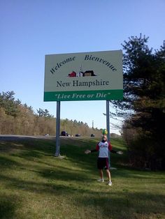 a man standing in front of a sign that says welcome to new hampshire, l'live free or die