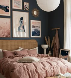 a bed with pink sheets and pillows in a bedroom next to pictures on the wall