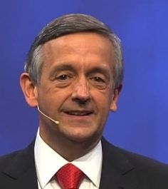 a man in a suit and tie smiles at the camera while wearing a headset