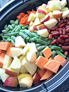 an assortment of fruits and vegetables are in a bowl together, including apples, carrots, beans, and broccoli