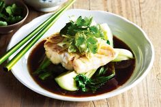 a white bowl filled with food next to chopsticks on top of a wooden table