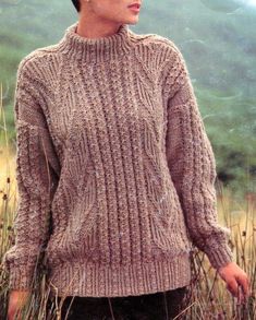 a woman standing in tall grass wearing a sweater