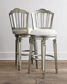 two metal bar stools with white upholstered cushions and backrests in front of a white wall