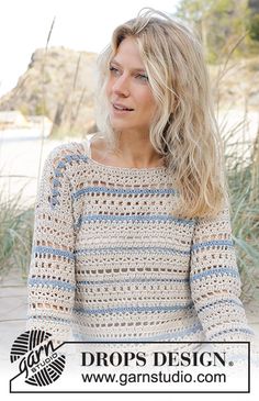 a woman wearing a crocheted sweater sitting in front of some grass and sand