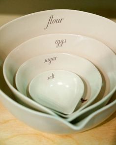 four white bowls stacked on top of each other with the words flour, eggs, sugar and salt written in cursive writing