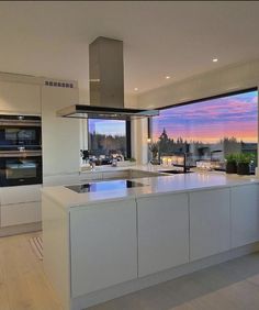 a large kitchen with an island counter top next to a window overlooking the water at sunset