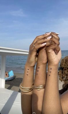 two women with matching tattoos on their arms holding each other's hands in front of the ocean