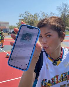 a woman holding up a cell phone in front of her face on a basketball court