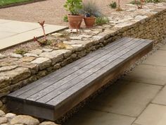 a wooden bench sitting on top of a stone wall next to potted planters