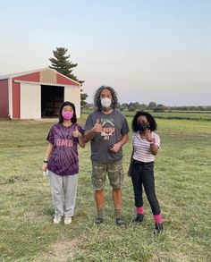 three people standing in a field wearing masks