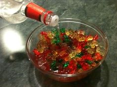 a glass bowl filled with gummy bears on top of a table next to a bottle