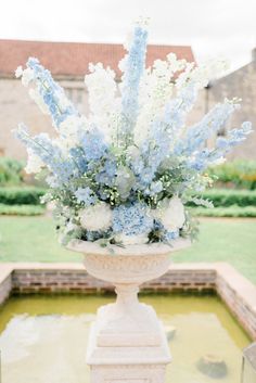 a vase with blue and white flowers sitting on top of a stone pedestal in the middle of a garden