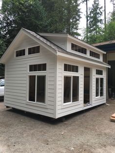 a small white house sitting on top of a dirt field next to a tree filled forest