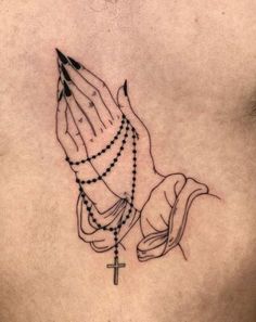 a woman's chest with a rosary and praying hands tattoo on her left side