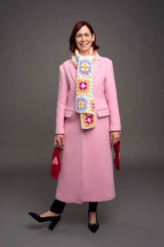 a woman in a pink coat and scarf is posing for a photo with her hands on her hips