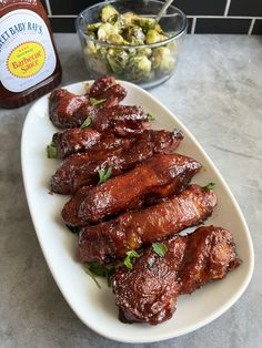 barbecued chicken wings on a white plate next to a bowl of salad