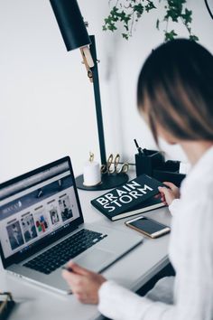 a woman sitting in front of a laptop computer on top of a desk next to a book