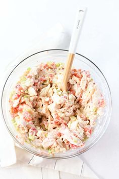 a glass bowl filled with chicken salad on top of a white tablecloth next to a wooden utensil