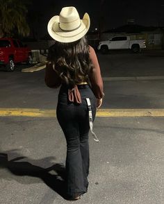 a woman in black pants and a white hat walking across a parking lot at night