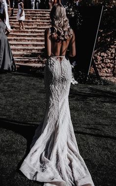 the back of a woman in a white wedding dress standing on grass with other people behind her