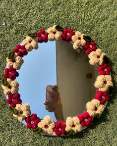 a hand holding a cell phone in front of a circular mirror with crocheted flowers