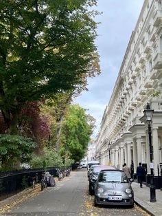 a car parked on the side of a street next to tall white buildings and trees