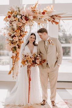 a bride and groom standing in front of a floral arch at their wedding ceremony venue