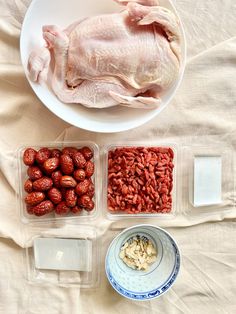 some food is sitting in plastic containers on a white tablecloth and next to a bowl with strawberries