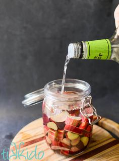 a person pouring water into a jar filled with sliced apples on top of a cutting board