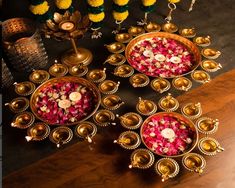 three metal bowls filled with flowers on top of a wooden table next to candles and vases