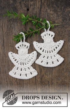 two crocheted angel ornament hanging from a tree branch on a wooden surface