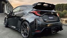 the rear end of a black sports car parked in front of a building with its trunk open