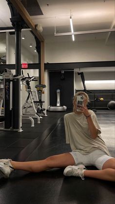 a woman sitting on the floor taking a selfie with her cell phone in a gym