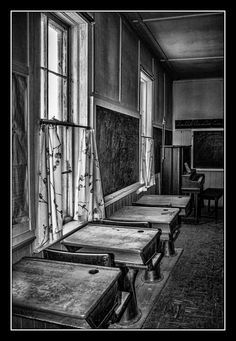 black and white photograph of old school desks in an empty room with chalkboard on the wall