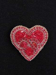 a red heart shaped brooch sitting on top of a black surface