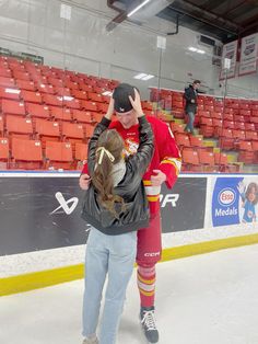 a man and woman hug on the ice in front of an empty hockey rink with red seats