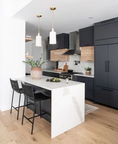 a modern kitchen with black cabinets and white countertops is featured in this image, along with two bar stools that match the wood flooring