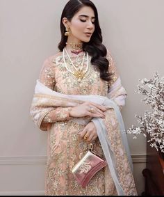 a woman in a pink and gold outfit holding a purse next to a vase with flowers