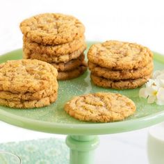 four cookies on a green plate next to a glass of milk and a white flower