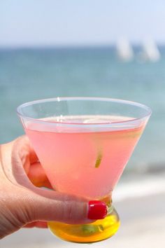 a person holding a pink drink in front of the ocean