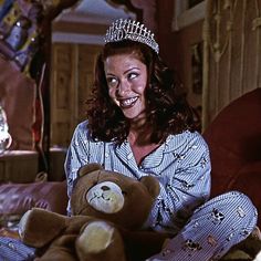 a woman wearing a tiara and holding a teddy bear in her lap, smiling at the camera