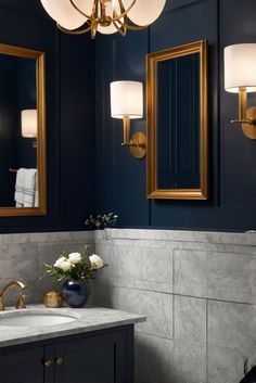 a bathroom with blue walls and marble counter tops, gold framed mirrors and two sinks