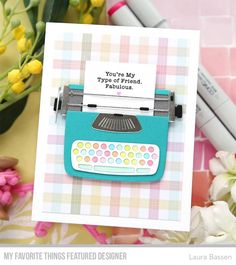 a close up of a card with a typewriter on it and flowers in the background