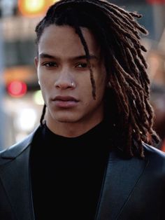 a young man with dreadlocks on his face and wearing a black shirt is standing in the street