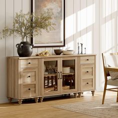 a wooden sideboard with glass doors and drawers in a living room area next to a painting on the wall