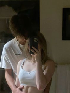 a man and woman standing in front of a mirror looking at their cell phones together