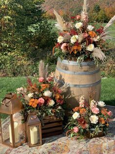 an arrangement of flowers and candles sitting on a table in front of a wooden barrel