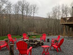 red chairs and fire pit in gravel area next to wooden deck with trees on hillside