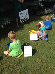 three children sitting on the grass playing with boxes and paper bags in front of them