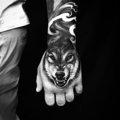 a man's arm with a wolf tattoo on it and his hand holding the wrist